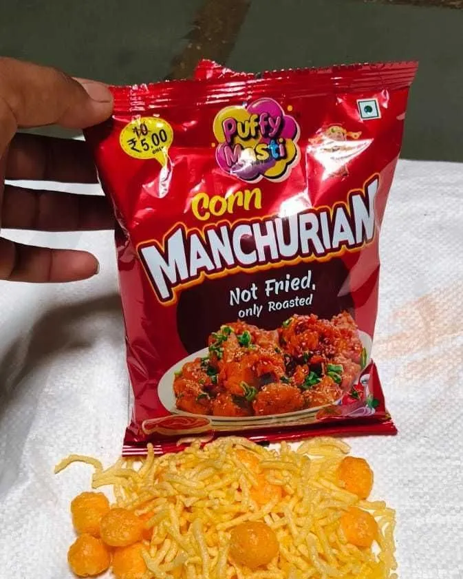 Corn Manchurian ₹5 packet from Puffy Masti, held in hand with the snack tipped out below